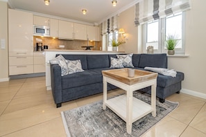 A modern kitchen with a microwave, coffee maker, and a dining area with a grey sofa and a small wooden table.