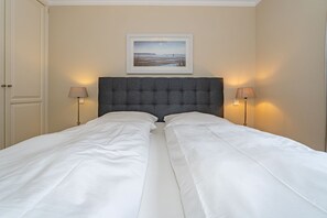 A double bed with a grey upholstered headboard, two bedside lamps, and a framed picture above the bed.