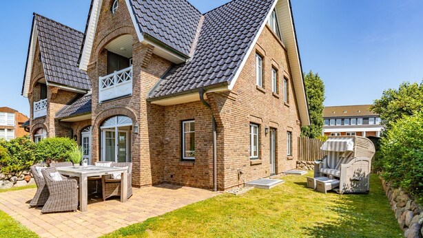 Una casa de dos pisos con fachada de ladrillo, un techo inclinado y un patio con mobiliario exterior.