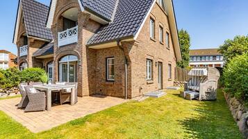 Ein zweistöckiges Haus mit Backsteinfassade, geneigtem Dach und einer Terrasse mit Gartenmöbeln.