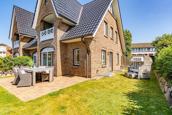 A two-story house with a brick exterior, a sloped roof, and a patio with outdoor furniture.