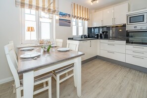 Eine moderne Küche mit weißen Schränken, einem Holzespeisetisch für vier Personen und einem großen Fenster mit gestreiften Vorhängen.
