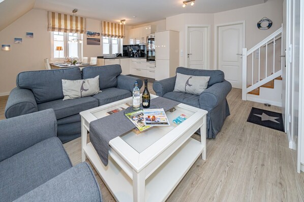 Ein modernes Wohnzimmer mit grauen Sofas, einem weißen Couchtisch und einer Küche im Hintergrund.