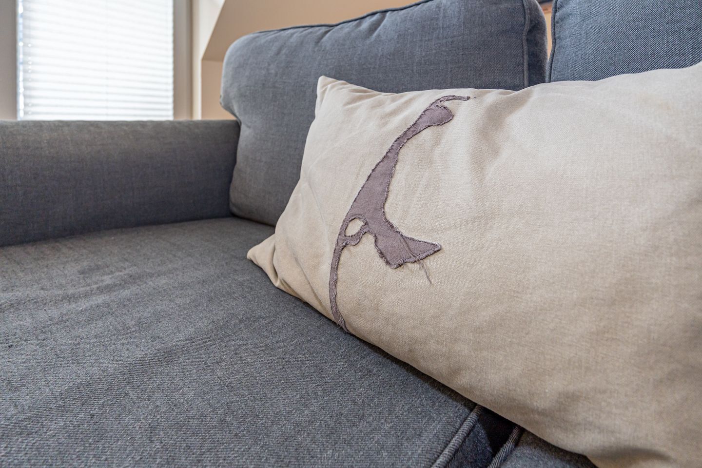 En grå soffa med en beige kudde som har ett broderat mönster.