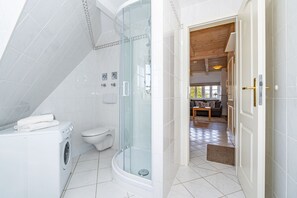A modern bathroom with a glass-enclosed shower, a toilet, and a washing machine. - Altstadttor App. 14 - Central 2-room apartment under thatch in Alt (Sylt)