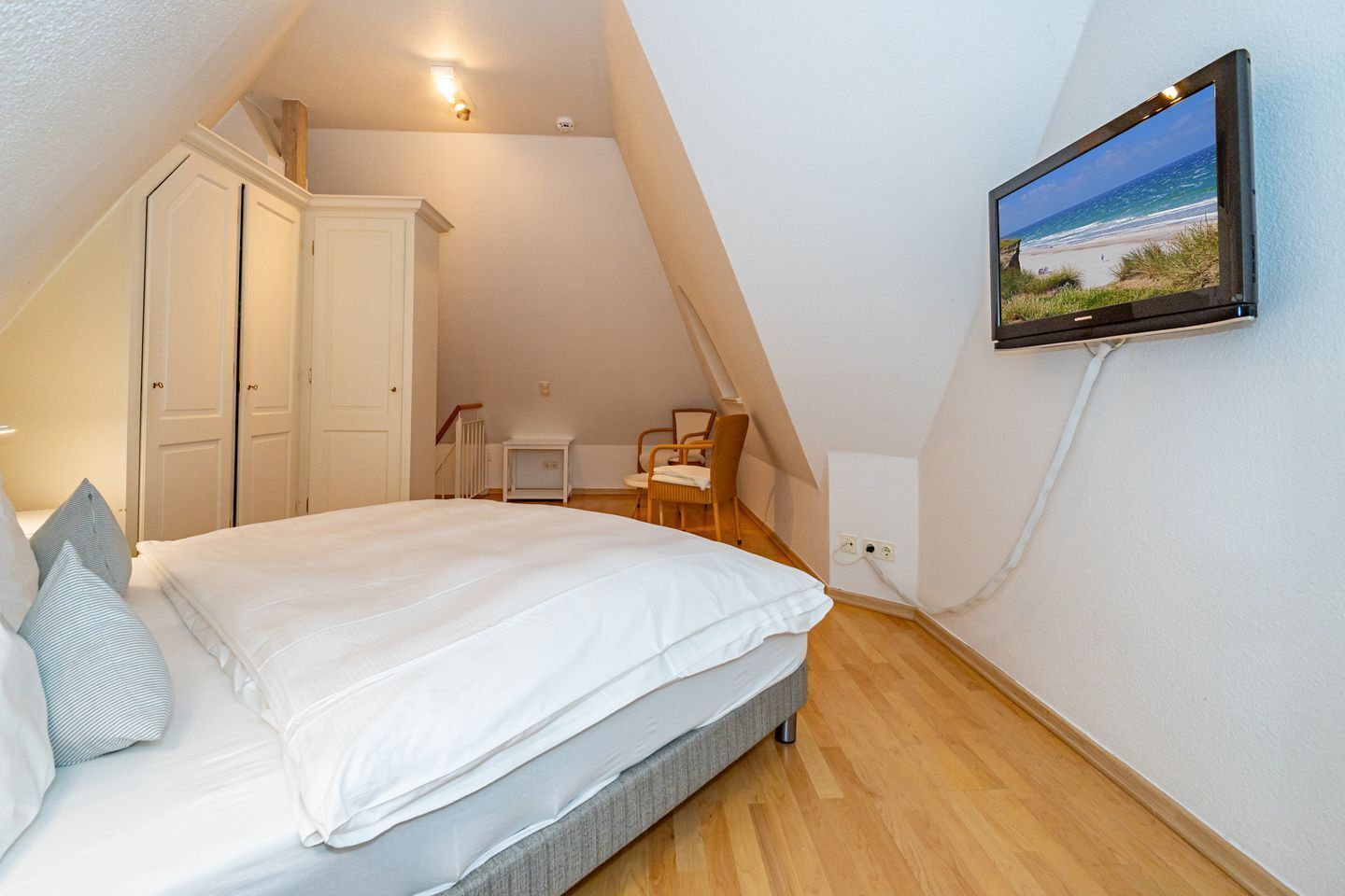 Ein Schlafzimmer mit einem Bett, einem Fernseher an der Wand und einem Schreibtisch mit Stuhl.