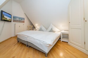 A bedroom with a bed, bedside tables, a radiator, and a painting on the wall. - Altstadttor App. 14 - Central 2-room apartment under thatch in Alt (Sylt)