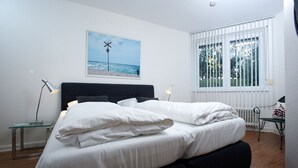 Un dormitorio con una cama grande, una mesita de noche, una lámpara, una ventana con persianas y un cuadro en la pared.