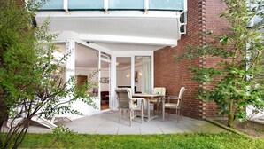Una casa moderna con un patio que incluye una mesa, sillas, un muro de ladrillo y un jardín.
