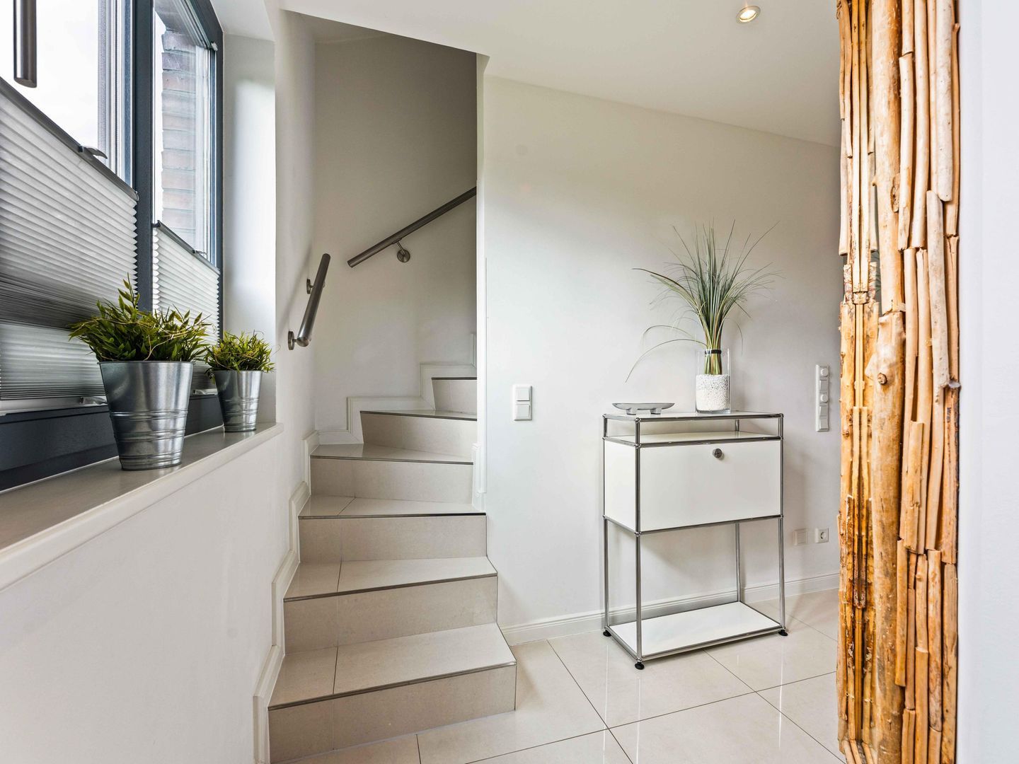A modern interior with a staircase, a metal-framed table with a plant, and a bamboo wall decoration.