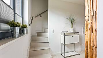 A modern interior with a staircase, a metal-framed table with a plant, and a bamboo wall decoration.