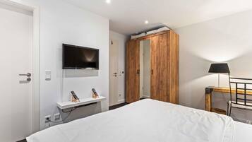 Une chambre d’hôtel comprenant un lit, un téléviseur fixé au mur, une armoire en bois, une table de chevet avec une lampe et un bureau avec un ordinateur.