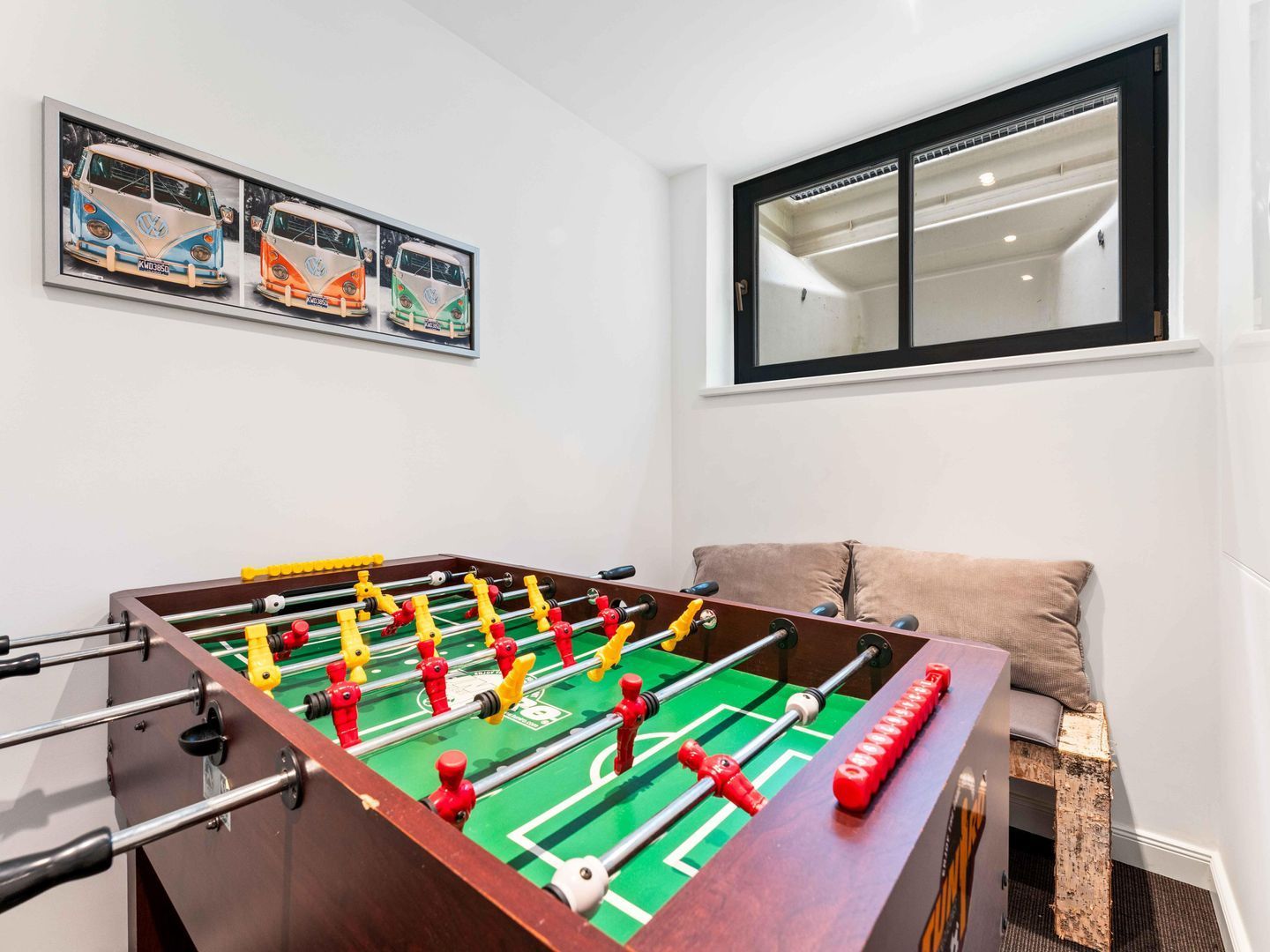 Une pièce avec une table de baby-foot, une fenêtre avec des stores et une œuvre d’art accrochée au mur.