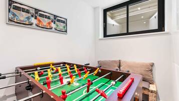 A room with a foosball table, a window with blinds, and a wall-mounted artwork.