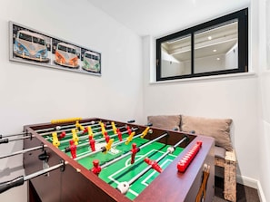 A room with a foosball table, a window with blinds, and a wall-mounted artwork.