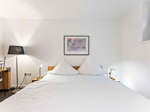 Une chambre d’hôtel avec un lit, un bureau, une lampe et une œuvre d’art encadrée au mur.