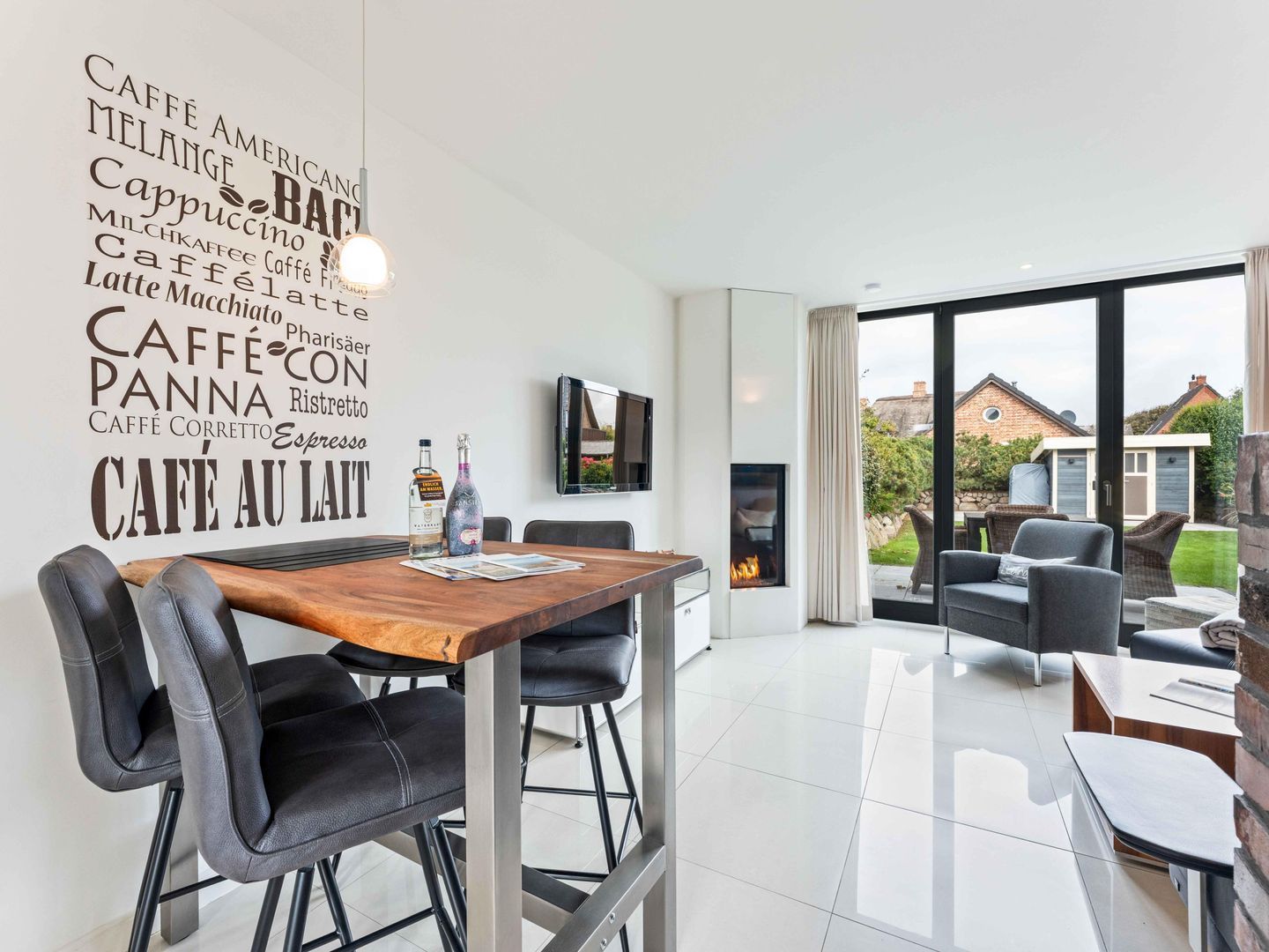 A modern kitchen with a wooden table and black chairs, a fireplace, and a large window with a view of houses.