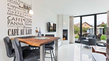 A modern kitchen with a wooden table and black chairs, a fireplace, and a large window with a view of houses.