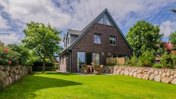 A two-story brick house with a sloped roof, a stone wall, and a well-maintained lawn.