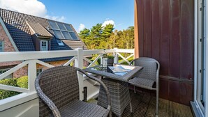 A balcony with wicker chairs and a table, overlooking a residential area with houses and trees. - Austernfischer App. 4 - 3-room apartment for up to 4 people with balcony. (Sylt)