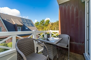 A balcony with wicker chairs and a table, overlooking a residential area with houses and trees.
