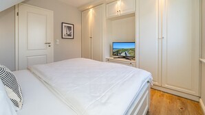 A bedroom with a bed, a television on a stand, and a wardrobe. - Austernfischer App. 4 - 3-room apartment for up to 4 people with balcony. (Sylt)