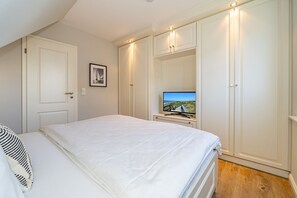 A bedroom with a bed, a television on a stand, and a wardrobe.
