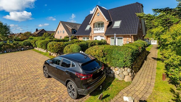 A modern two-story house with a paved driveway and a parked car. - Austernfischer App. 4 - 3-room apartment for up to 4 people with balcony. (Sylt)