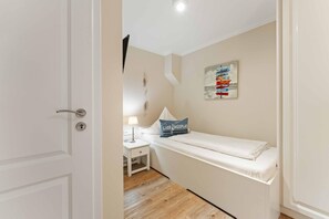 Ein kleines, ordentlich eingerichtetes Schlafzimmer mit einem Einzelbett, einem Nachttisch mit Lampe und einem an der Wand befestigten Schild.