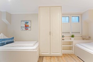 A bedroom with a bed, a wardrobe, a window with blinds, a small shelf with decorative items, and a wall art piece.
