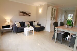 Una sala moderna con un sofá gris, una mesa de centro blanca y una mesa de comedor con sillas de mimbre.