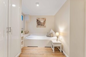Una habitación pequeña y bien iluminada con una cama, mesita de noche y una obra de arte colgada en la pared.