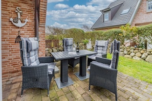 Eine Terrasse im Freien mit Backsteinmauer, Tisch und vier Stühlen.