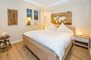 Ein Schlafzimmer mit einem hölzernen Bett, einer Weltkarte an der Wand, einem Fenster mit Jalousien, einer Lampe auf dem Nachttisch und einem kleinen Hocker mit einer Schaf-Figur.
