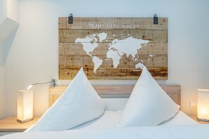 Ein Schlafzimmer mit einer Wanddekoration aus einer Holz-Weltkarte, zwei Nachttischlampen und einem Bett mit weißen Kissen.