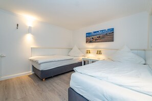 Ein Hotelzimmer mit zwei Betten, einem Nachttisch mit Lampen, einem Gemälde mit Strandmotiv und Holzboden.