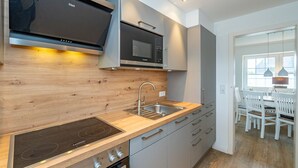 A modern kitchen with a wood backsplash, stainless steel appliances, and a built-in oven. - Nordersuite - Just behind the dunes. 4-room vacation apartment in the north of (Sylt)