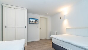 A bedroom with a bed, a wardrobe, a wall-mounted TV, and a radiator. - Nordersuite - Just behind the dunes. 4-room vacation apartment in the north of (Sylt)