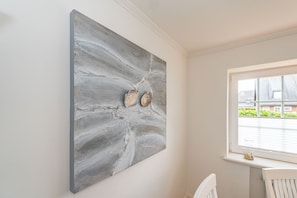 Ein Zimmer mit einem großen, abstrakten Gemälde an der Wand, einem Fenster mit Blick auf Gebäude und einem weißen Stuhl.