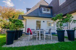 Une maison dotée d’un patio comprenant une table et des chaises, le tout agrémenté de plantes en pot.