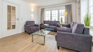 A modern living room with a glass coffee table, two grey sofas, and a grey armchair. - Nordersuite - Just behind the dunes. 4-room vacation apartment in the north of (Sylt)