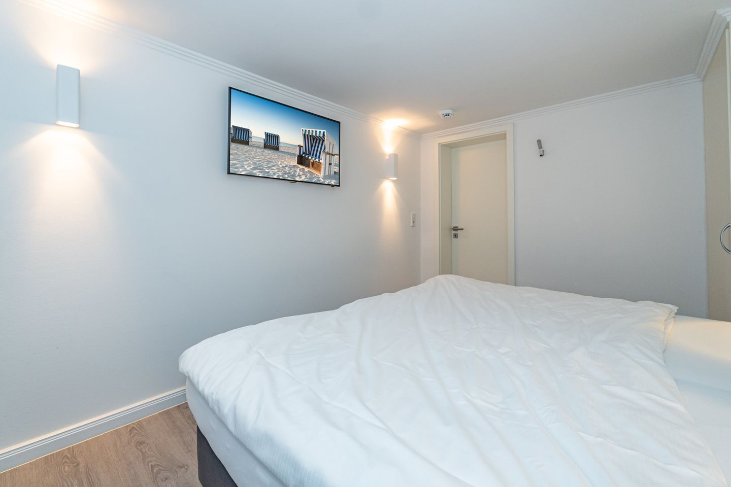 A bedroom with a bed, a wall-mounted picture, and two wall sconces.