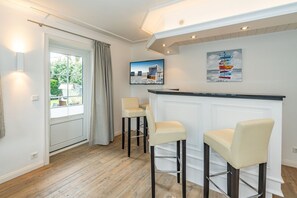Une cuisine moderne avec un plan de travail blanc, trois tabourets de bar et une grande fenêtre agrémentée de rideaux.