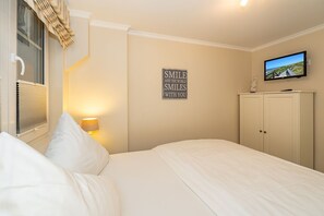 A bedroom with a bed, a wall-mounted TV, a bedside lamp, a wardrobe, and a motivational quote on the wall. - Auszeit Sylt App. 2 - Hier ist der Name Programm, Nehmen Sie Sich Eine Auszeit auf Sylt (Sylt)