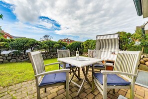An outdoor patio with a table and chairs, a grill, and a stone wall. - Auszeit Sylt App. 2 - Hier ist der Name Programm, Nehmen Sie Sich Eine Auszeit auf Sylt (Sylt)
