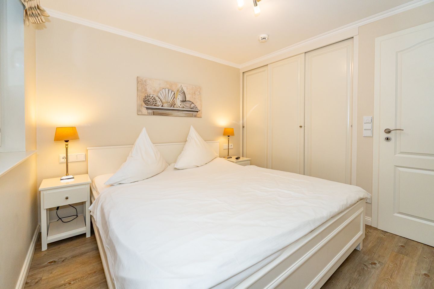 Ein ordentlich eingerichtetes Schlafzimmer mit einem großen Bett, zwei Nachttischen mit Lampen, einem Wandbild und einem Kleiderschrank.