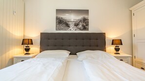 A double bed with white linens, two bedside lamps, a grey upholstered headboard, and a black and white landscape painting above the bed. - Stadtresidenz App. 4 - Ebenerdige, Moderne Stadtwohnung- Kurze Wege zum Strand, mit Eigener (Sylt)