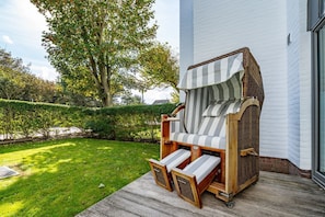 A wooden deck chair with striped cushions and a woven canopy, positioned on a wooden deck in front of a white building. - Stadtresidenz App. 4 - Ebenerdige, Moderne Stadtwohnung- Kurze Wege zum Strand, mit Eigener (Sylt)