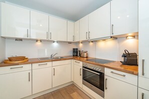 A modern kitchen with white cabinets, a wooden countertop, a Bosch oven, and a coffee maker.