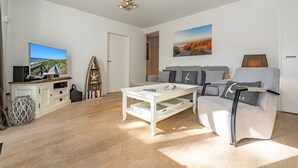 A modern living room with a flat-screen TV, a white coffee table, a grey sofa, and a bookshelf. - Stadtresidenz App. 4 - Ebenerdige, Moderne Stadtwohnung- Kurze Wege zum Strand, mit Eigener (Sylt)